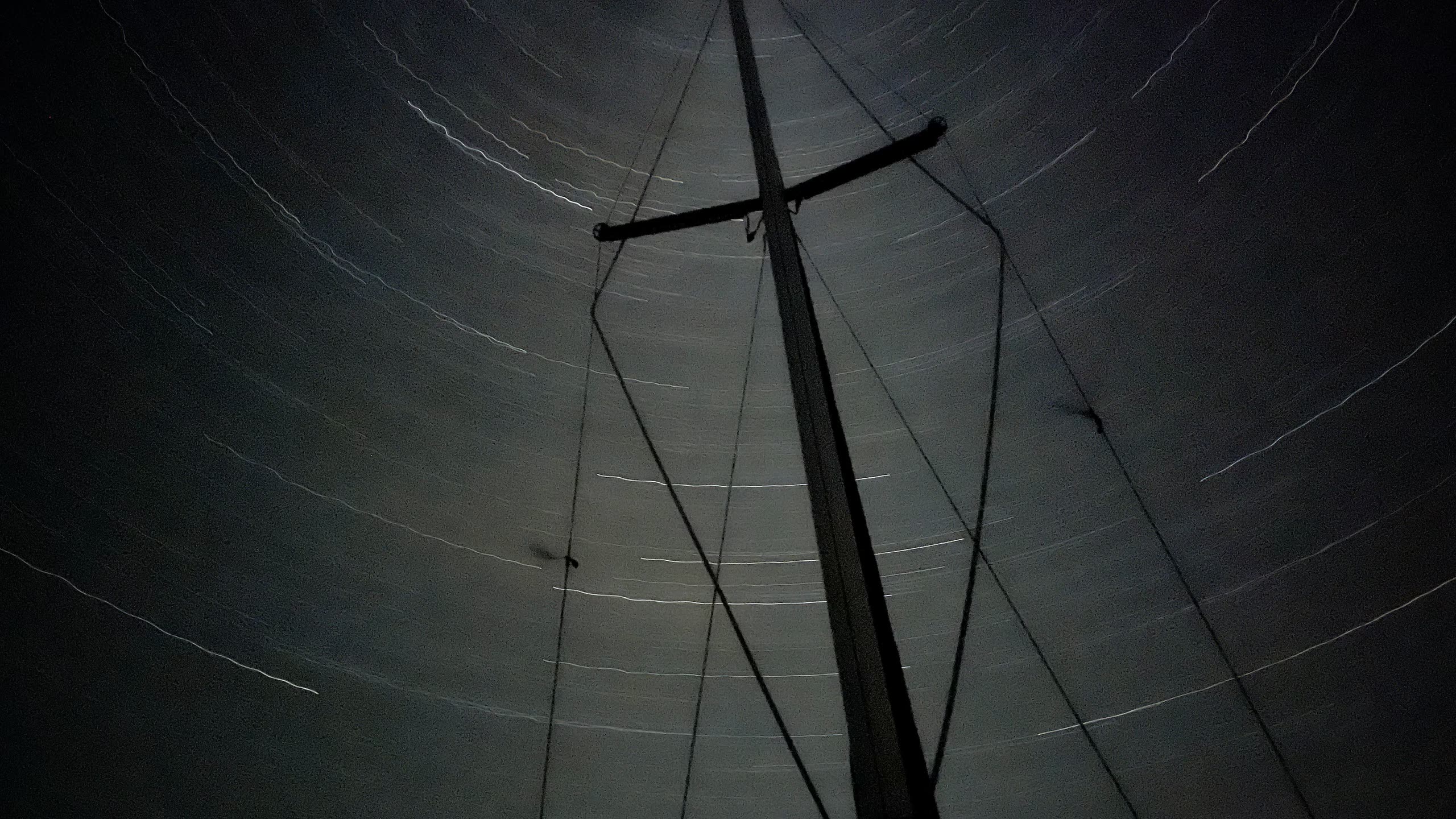 Long-exposure photograph looking up the mast of a sailboat at night. Star trails arc concentrically around the celestial pole against a dark sky.