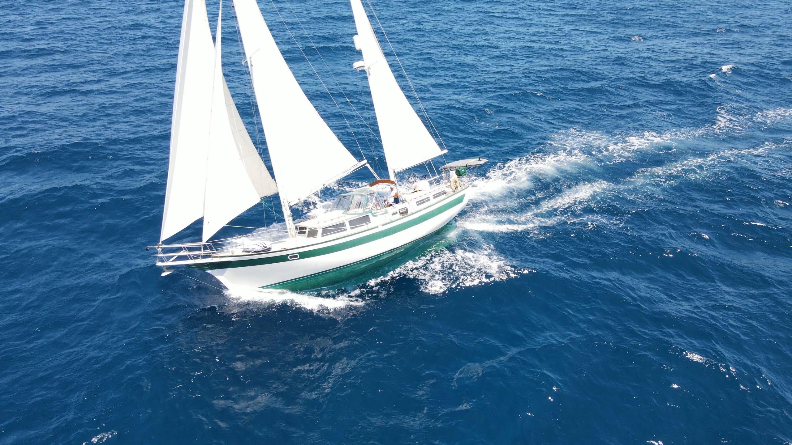 Aerial photograph of the sailboat Shearwater under full sail on deep blue water, seen from above and slightly ahead.